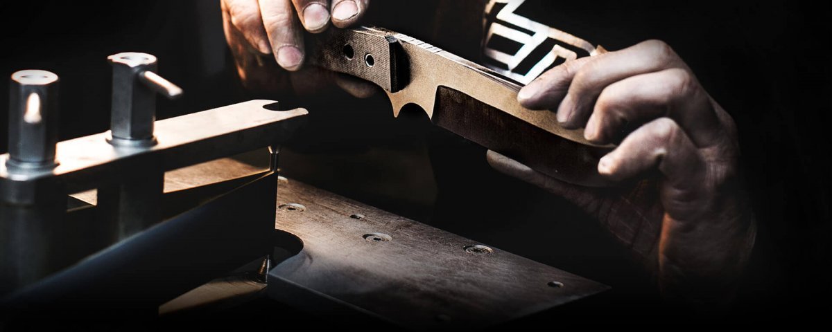 Master craftsman handcrafting TRC knife blade in Lithuanian workshop with precision tools and dramatic lighting